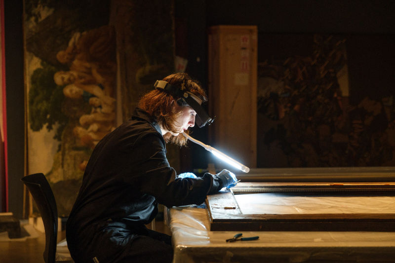 A woman looking at a painting with magnifying googles