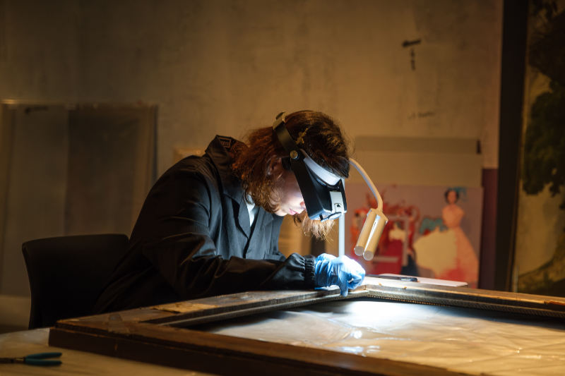 A woman looking at a painting with magnifying googles
