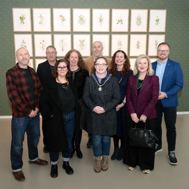 A group of people in front of a grid of paintings.