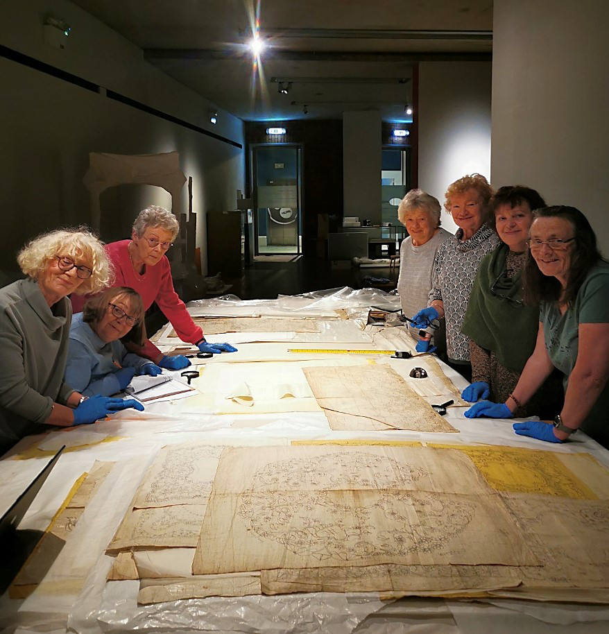 A group of women around a table with lace patterns.